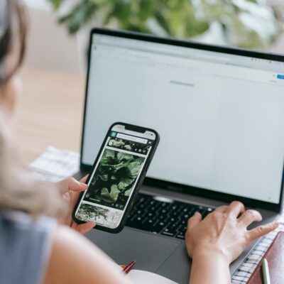 Content creator looking at plants on phone while working at a laptop
