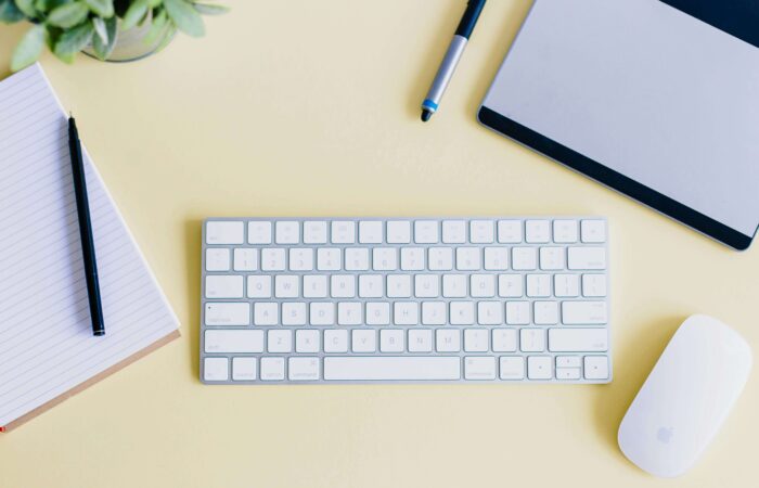 birds eye view of an apple keyboard, mouse and notepad on a yellow desk