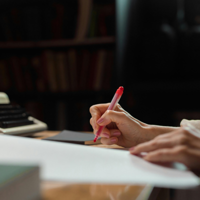 Woman's hand holding a red pen above a document at a desk